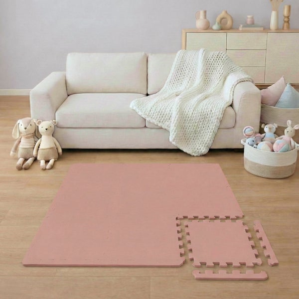 Hell eingerichtetes Wohnzimmer mit einer rosa Schaumstoff-Puzzlematte auf Holzboden vor einem hellen Sofa mit Decke und Spielzeug.
