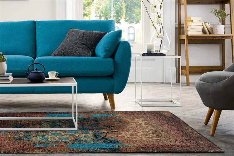 Wohnzimmer mit blauem Sofa, modernem Couchtisch, Beistelltisch und einem Teppich mit Vintage Muster in einem hellen, einladenden Ambiente.