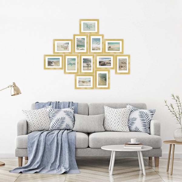 Wohnzimmer mit grauem Sofa und einer Bildergalerie aus zwölf goldfarbenen Bilderrahmen an der Wand mit maritimen Strandmotiven.