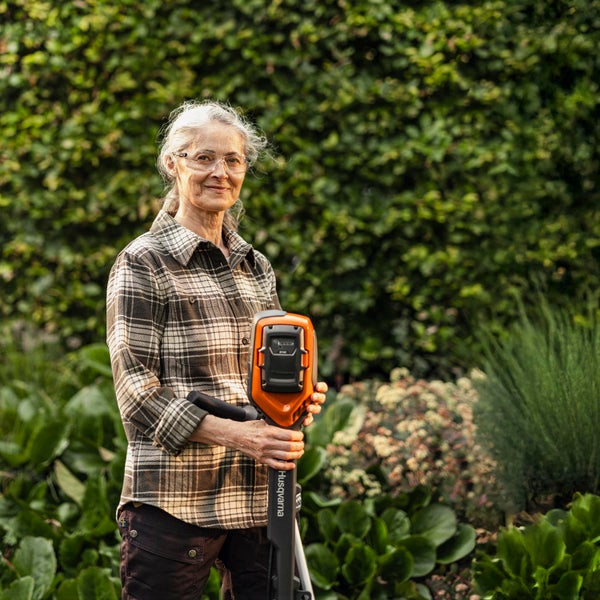 Frau hält Husqvarna Rasentrimmer im Garten