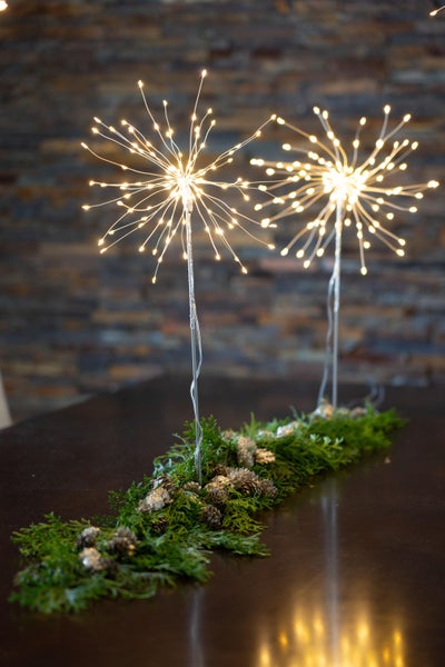 Zwei Deko-Leuchten in Sternform mit Tannengrün und Zapfen auf einem Tisch