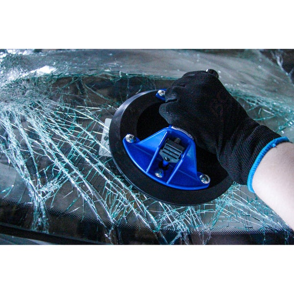 Eine Hand mit Handschuh verwendet einen Glassauger auf einer zerbrochenen Windschutzscheibe.