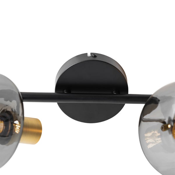 Nahaufnahme einer schwarzen Wandleuchtenhalterung mit einem Metallstab und zwei Lampenschirmen aus Rauchglas mit messingfarbenen Fassungen.