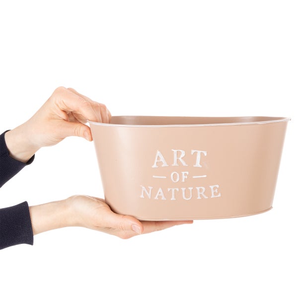 Beige ovaler Pflanzkübel aus Metall mit weißem Text Art Of Nature, zur Veranschaulichung der Größe in den Händen gehalten.