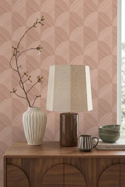Strukturierte Tapete in Rosé mit Bogenmuster in einem hellen Zimmer auf einer Holzkommode mit Tischlampe und Keramikvase.