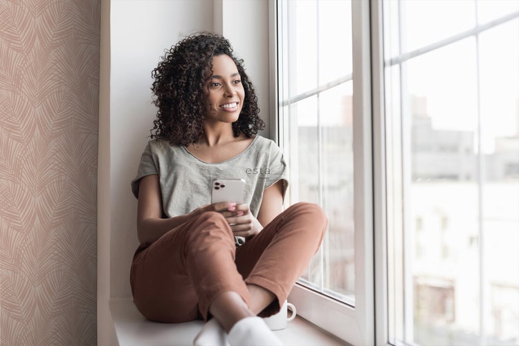 Eine Frau sitzt am Fenster mit einer Tapete mit tropischen Blättern.