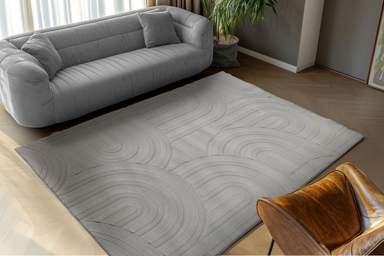 Wohnzimmer mit modernem Design, grauer Teppich mit geometrischem Bogenmuster, Sofa und Ledersessel auf Parkettboden.