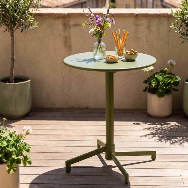 Runder Bistrotisch aus Metall auf einer sonnigen Terrasse mit Holzdeck, Blumen und Snacks.