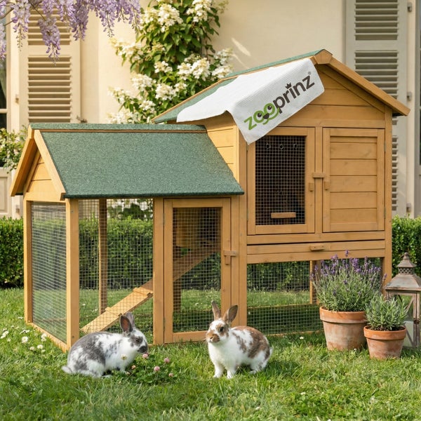 Zweistöckiger Kaninchenstall aus Holz mit Freilaufgehege, Rampe und wetterfestem Dach in einem hellen Garten. zooprinz Logo.