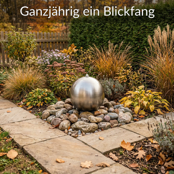 Edelstahl-Kugelbrunnen auf Natursteinen in einem Garten mit Ziergräsern, Stauden und einem Steinplattenweg.