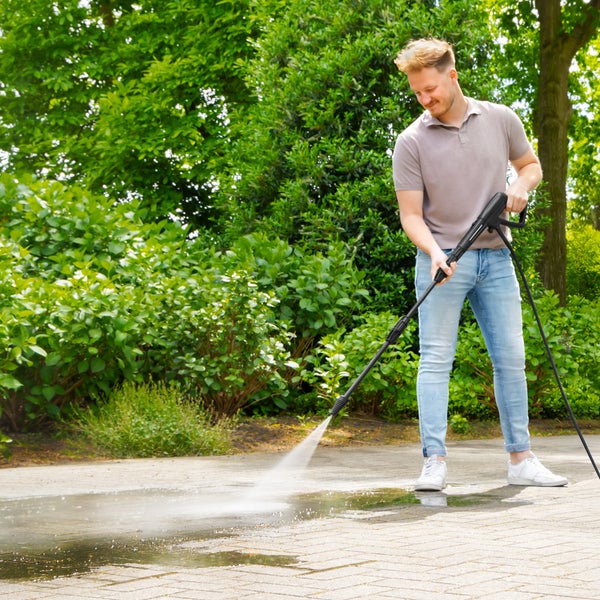 Ein Mann reinigt mit einem Hochdruckreiniger eine gepflasterte Fläche im Freien.