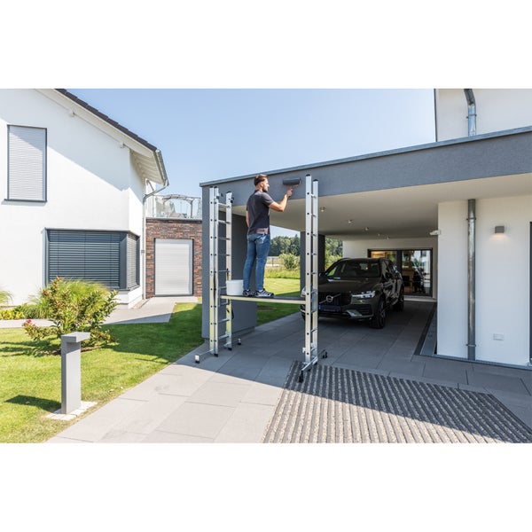 Mann streicht Hauswand von einem Fahrgerüst aus.