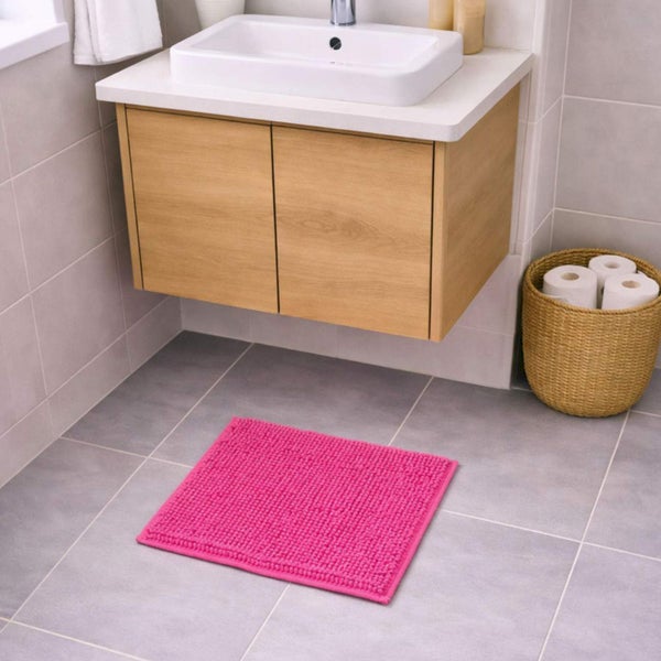 Quadratische, strukturierte Badematte in Pink auf Bodenfliesen vor einem Waschtisch aus Holz in einem hellen Badezimmer.