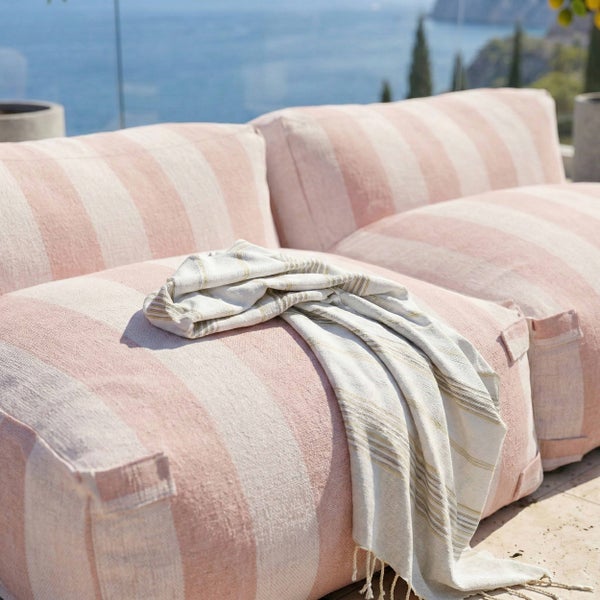 Gestreifte Outdoor-Loungekissen auf einer hellen Terrasse mit Meerblick und einer Wohndecke.