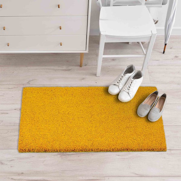 Gelbe Fußmatte neben Kommode und Schuhen auf hellem Holzboden.