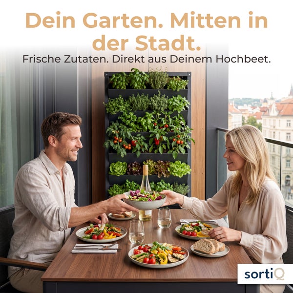 Ein Paar isst auf einem Stadtbalkon an einem Holztisch, im Hintergrund steht ein vertikales Hochbeet mit frischen Kräutern und Gemüsepflanzen.
