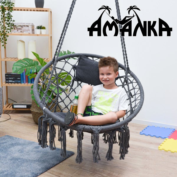 Junge sitzt in einem grauen Hängesessel mit Kissen und Fransen vor einer Wand mit dem Amanka Logo.