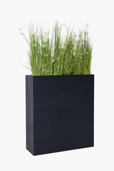 Hoher, rechteckiger Pflanzkübel in dunkler Optik mit künstlichem Gras und kleinen weißen Blüten.