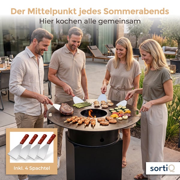 Zwei Paare bereiten gemeinsam Grillgut auf einer runden Feuerplatte mit integrierter Grillfläche zu, inklusive vier Edelstahlschaber mit Holzgriff.