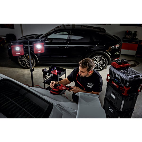 Ein Handwerker nutzt eine kabellose FLEX Poliermaschine zur Autopflege in einer Werkstatt mit professioneller Beleuchtung und Stapelboxen.