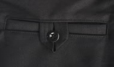 Nahaufnahme einer Paspeltasche mit Knopfverschluss und Stofflasche an schwarzer Arbeitskleidung.