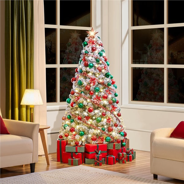 Weihnachtsbaum mit roter und grüner Dekoration sowie Geschenken in einem Wohnzimmer.