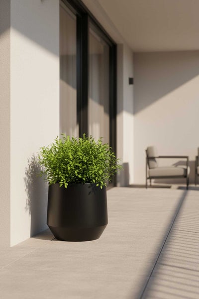 Schwarzer Pflanzkübel mit grüner Pflanze auf einer hellen Terrasse.
