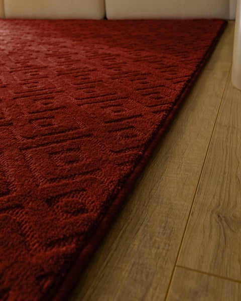Roter strukturierter Teppich mit geometrischem Muster auf einem Boden in Holzoptik.