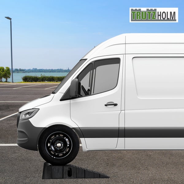 Weißer Transporter mit Vorderrad auf schwarzem Auffahrkeil von Trutzholm auf einem Parkplatz im Freien. Trutzholm Logo.