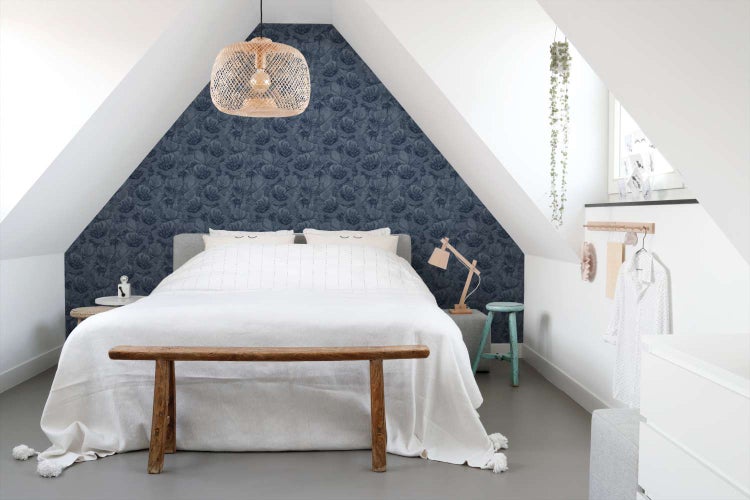 Schlafzimmer mit Dachschräge, tapeziert mit dunkelblauer Blumentapete, helles Bett, Holzhocker und geflochtene Hängelampe in modernem Wohnstil.