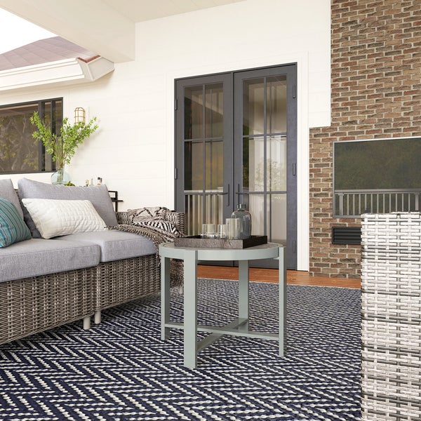 Eine Terrasse mit einem grauen Sofa, einem grauen Tisch und einem blau-weiß gemusterten Teppich.