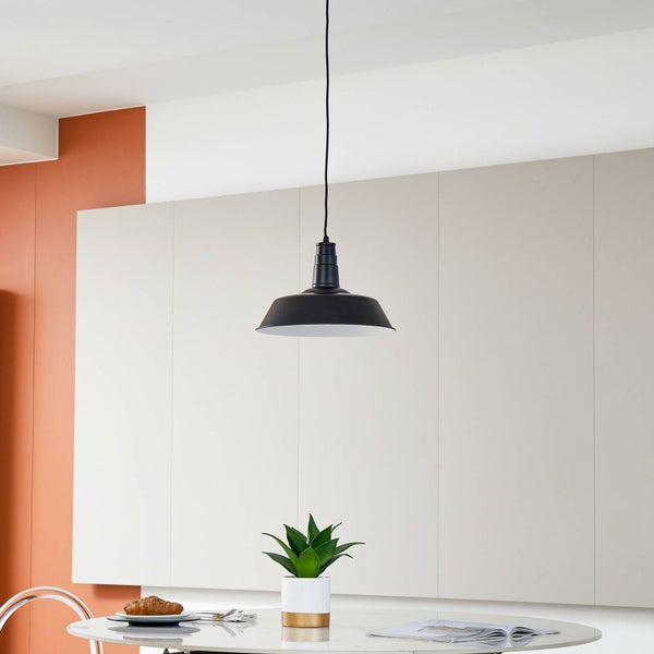 Pendelleuchte aus Metall in Schwarz über einem runden Esstisch mit Pflanze und Gebäck in einem modernen Wohnraum.