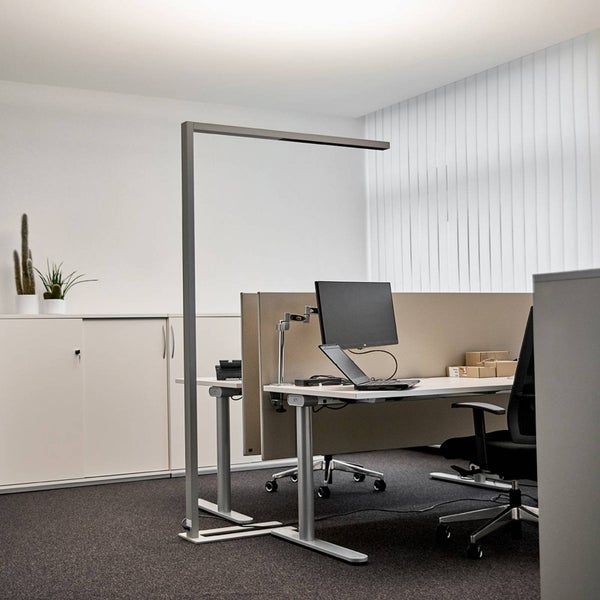 Moderner Büroarbeitsplatz mit Schreibtisch, Monitor, Bürostuhl und einer großen, minimalistischen LED-Stehleuchte in Silber.