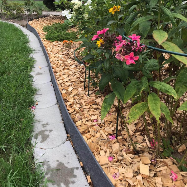 Rasenkante aus Kunststoff trennt eine Rasenfläche von einem Beet mit Holzhackschnitzeln und Blumen.