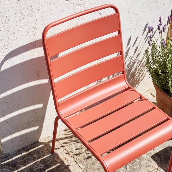 Moderner terrakottafarbener Gartenstuhl aus Metall mit Querlattung, auf einer Terrasse neben einem Tontopf mit Lavendel.