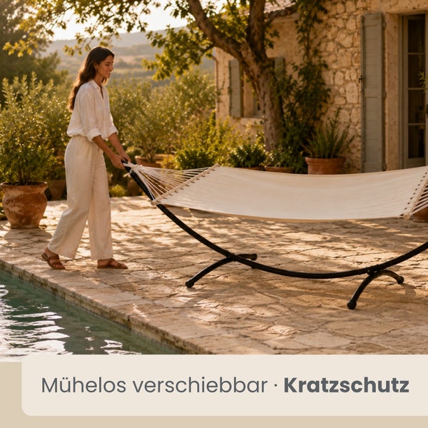Eine Frau verschiebt eine Hängematte mit schwarzem Metallgestell auf einer sonnigen Naturstein-Terrasse neben einem Pool.