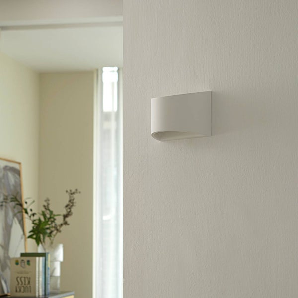 Weiße, geschwungene Wandleuchte aus Gips in einem hellen, modern eingerichteten Raum an einer Wand montiert.