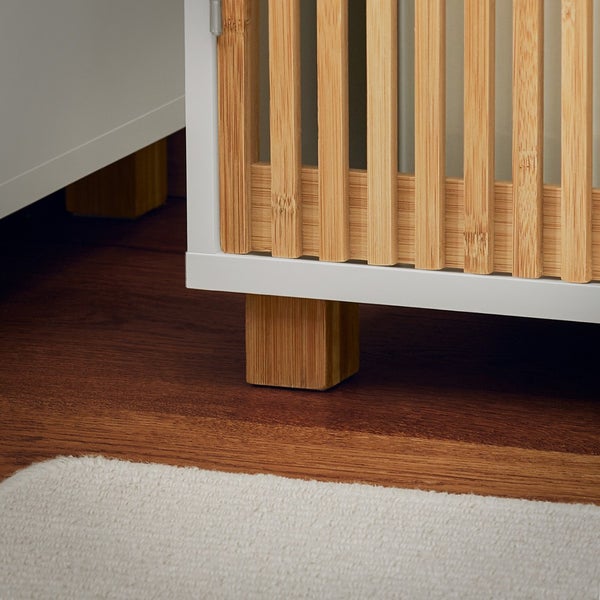 Detailaufnahme eines weißen Schranks mit Bambuselementen und Holzfüßen.