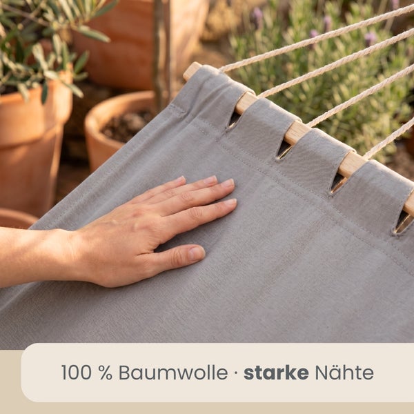 Hand auf dem Stoff einer Hängematte aus 100 Prozent Baumwolle mit starken Nähten in einem hellen Garten.