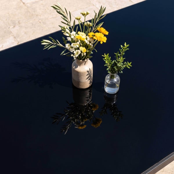 Zwei Vasen mit Blumen auf einer dunklen, stark reflektierenden Tischplatte im Außenbereich.