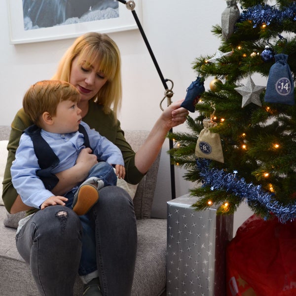 Eine Frau hält ein Kind auf dem Schoß und gemeinsam betrachten sie den mit kleinen Adventskalendersäckchen geschmückten Weihnachtsbaum.