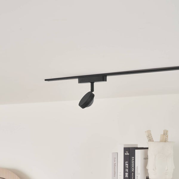 Schwarzes Schienensystem mit einem verstellbaren LED-Strahler an einer weißen Decke über einem Regal.