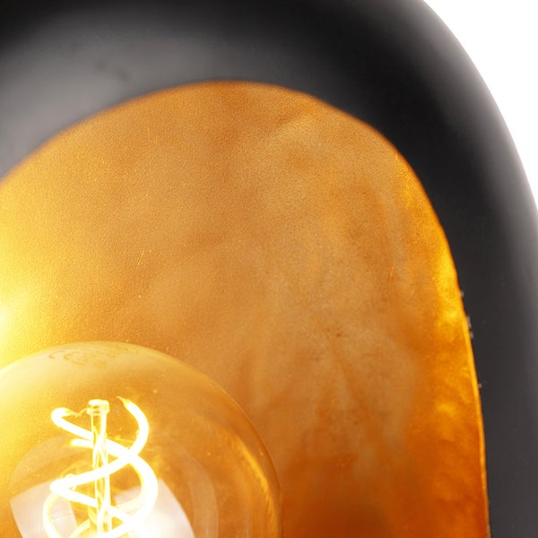 Nahaufnahme einer Glühbirne vor einem schwarzen Lampenschirm mit goldfarbener Innenseite