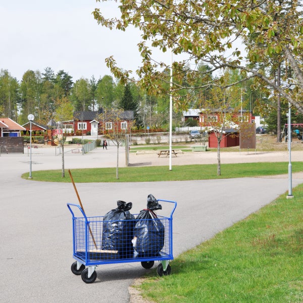 Blauer Gitterwagen mit Müllsäcken und Besen auf einem Gelände.
