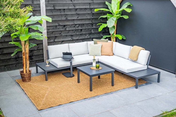 Modernes Garten-Lounge-Set mit anthrazitfarbenem Gestell und hellgrauen Polstern, bestehend aus Ecksofa, Couchtisch und Teppich auf einer Terrasse.