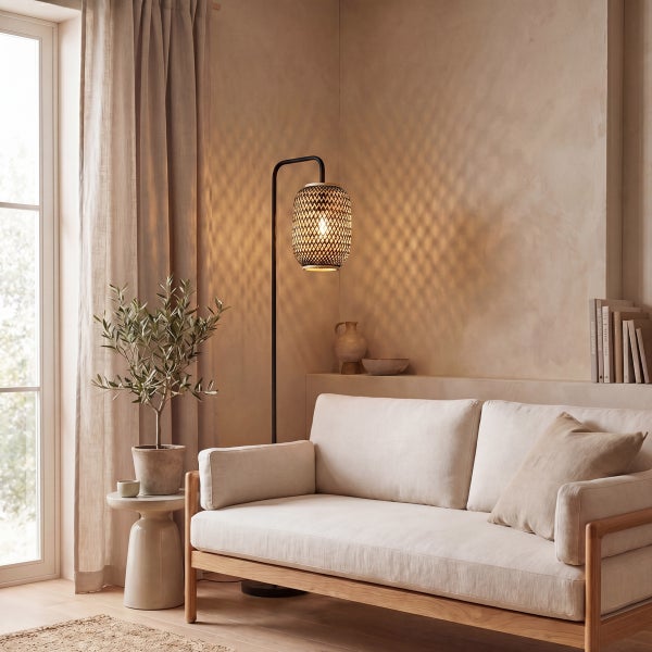 Moderne Stehleuchte mit Rattanschirm neben einem Sofa in einem gemütlich eingerichteten Wohnzimmer mit Naturmaterialien.