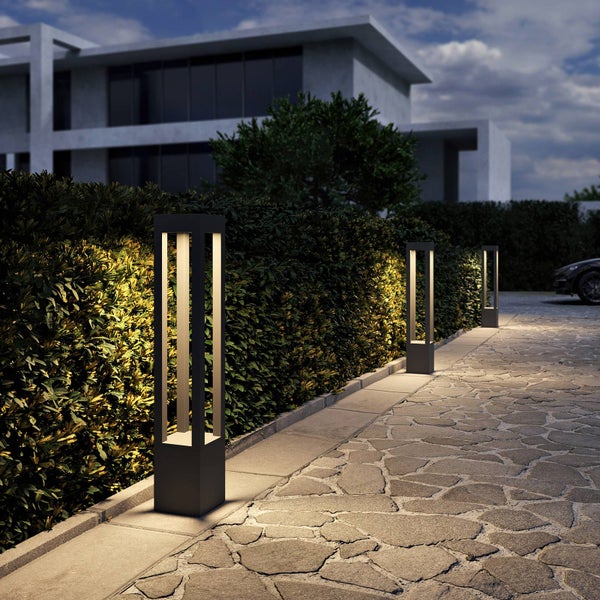 Moderne LED-Sockelleuchten aus dunklem Metall beleuchten einen gepflasterten Gartenweg neben einer Hecke bei Dämmerung.