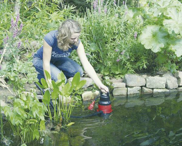 Frau bedient eine Teichpumpe in einem Gartenteich.