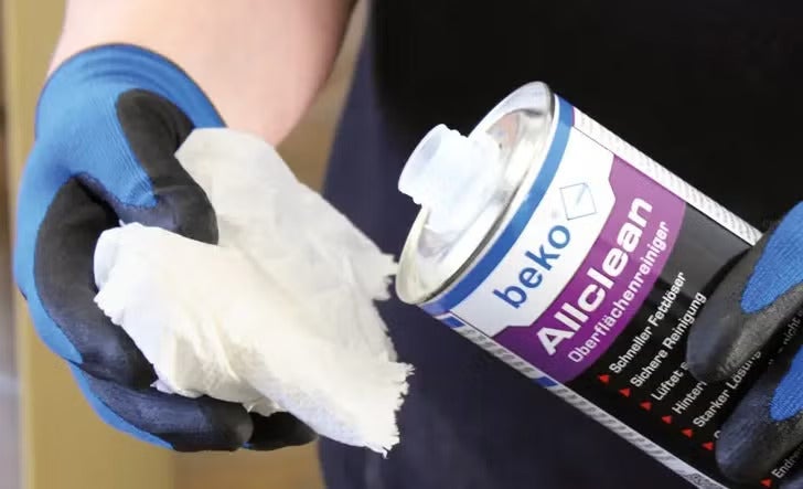 Eine Person mit Arbeitshandschuhen trägt beko Allclean Oberflächenreiniger auf ein Tuch auf.