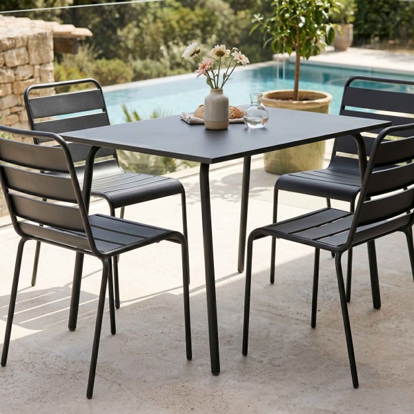 Modernes Gartenmöbel-Set aus dunklem Metall mit rechteckigem Tisch und vier Stapelstühlen auf einer hellen Terrasse am Pool.